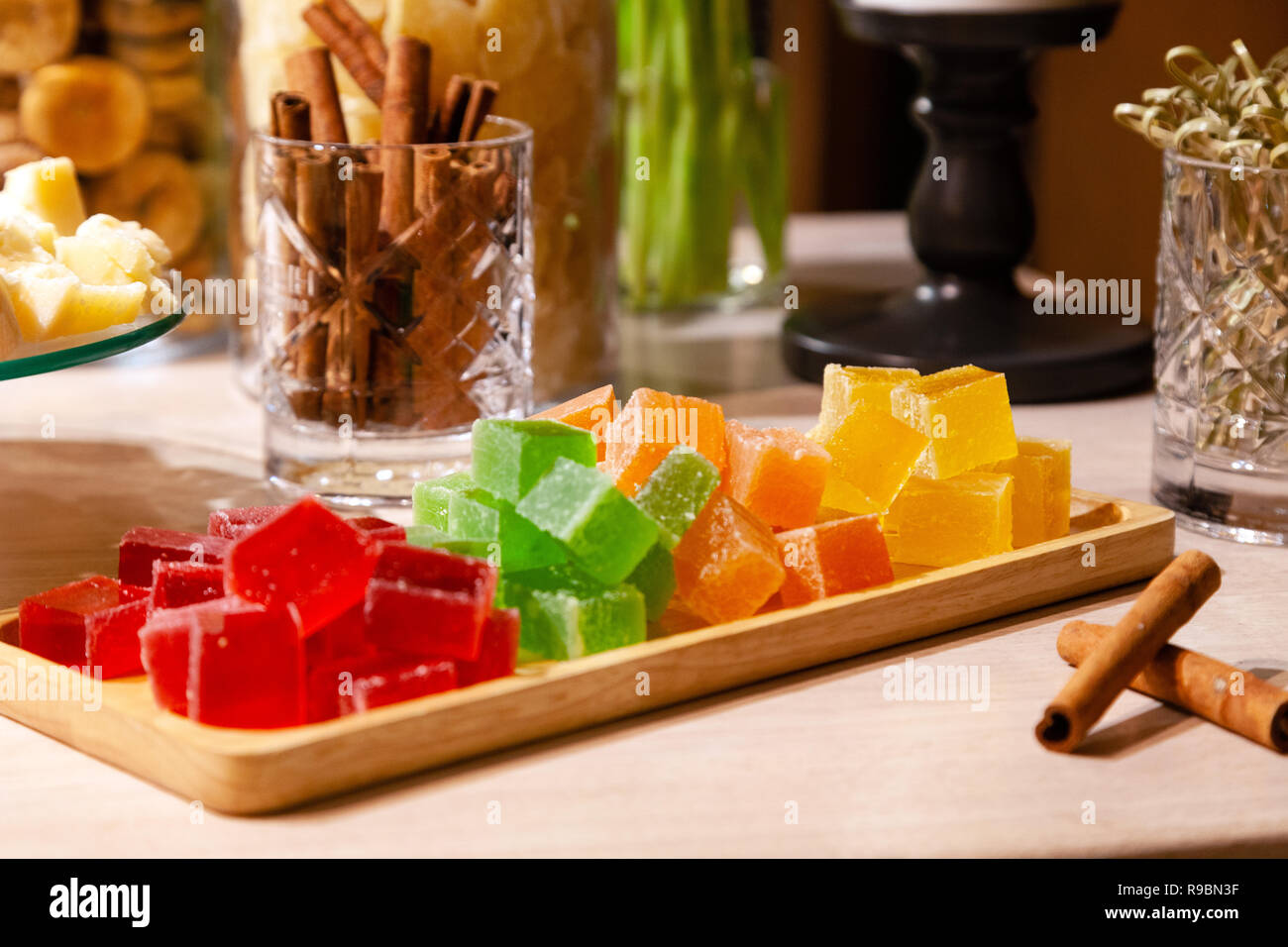 Libre de piles de petits cubes de vert, rouge, jaune, la marmelade d'orange et des bâtons de cannelle dans le verre cristal sur la plaque en bois rectangulaire sur un caterin Banque D'Images