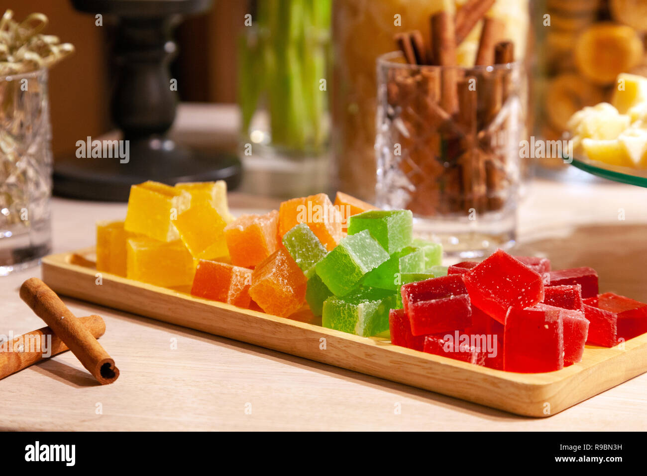 Libre de piles de petits cubes de vert, rouge, jaune, la marmelade d'orange  et des bâtons de cannelle dans le verre cristal sur la plaque en bois  rectangulaire sur un caterin Photo