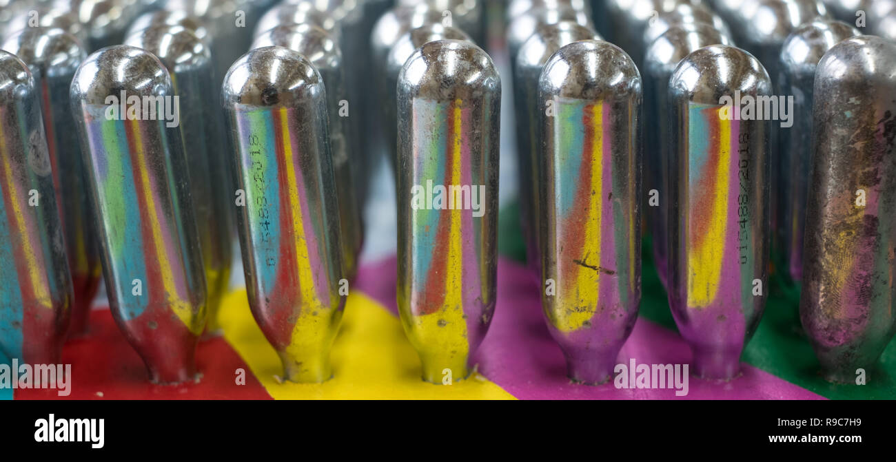 L'oxyde nitreux cannisters vide reflétant couleurs psychédéliques : cylindres de métal contenant de l'oxyde nitreux, utilisé pour la crème à fouetter, mais aussi comme un cadre juridique Banque D'Images