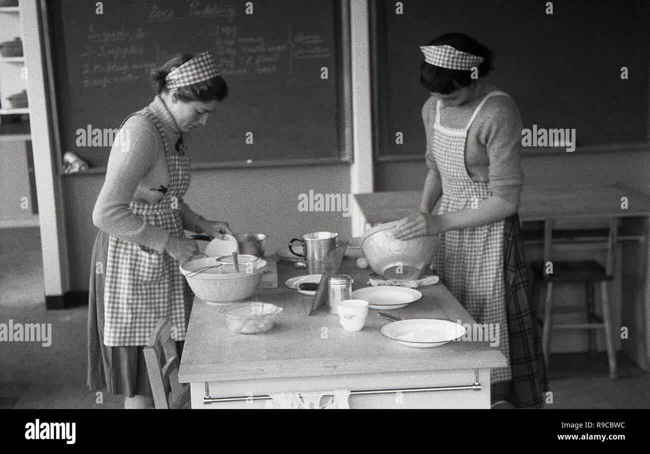 Années 1950, historiques, des tabliers et des écolières dans peu de filets à cheveux faire côté cuisine dans une classe, England, UK. En cette ère, accueil classes économiques étaient une partie importante du programme scolaire pour les élèves. Banque D'Images