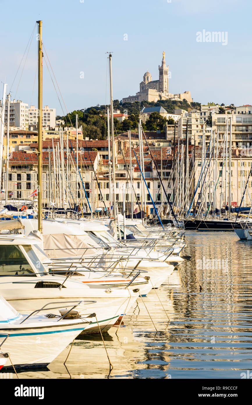 Les bateaux de plaisance amarrés dans le port de plaisance du Vieux Port de Marseille, France, avec la basilique Notre-Dame de la garde en haut de la colline au coucher du soleil. Banque D'Images