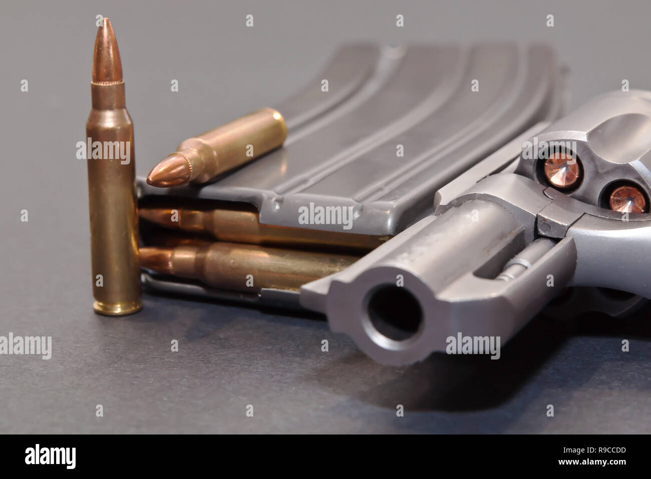 Magazine un fusil chargé avec des balles de calibre 0,223 et deux autres en plus à côté d'un acier inoxydable 357 revolver sur fond gris Banque D'Images