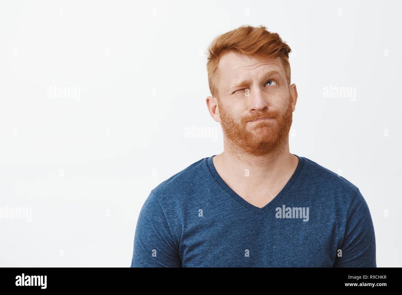 Redhead attractive male avec en soie bleu occasionnels t-shirt, à la recherche des lèvres de son, hmm la fermeture d'un œil et à la pensée, ou la prise de décision, en essayant de calculer à l'esprit ou l'idée de faire Banque D'Images