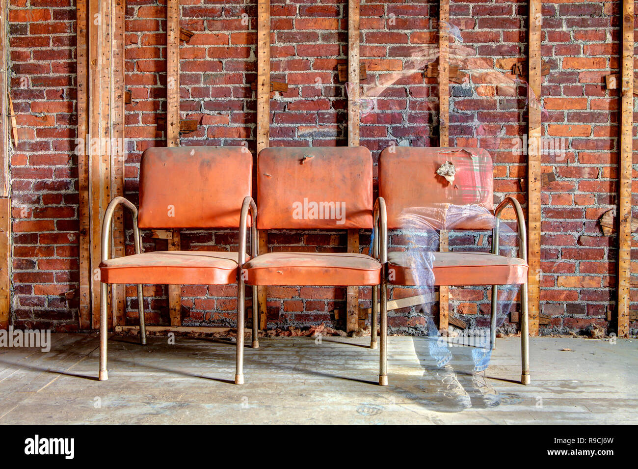 L'image fantomatique d'un homme assis sur une chaise orange décoloré voir-à travers des corps en bâtiment abandonné. Banque D'Images