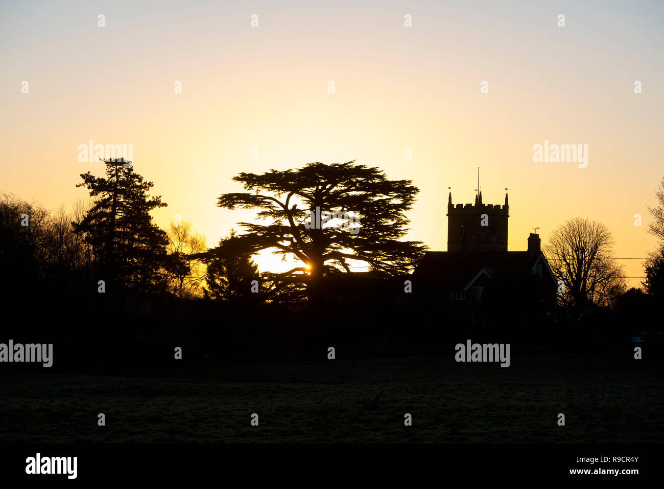 St Laurence's Church tower derrière une maison au lever du soleil en hiver. Combe, Oxfordshire, Angleterre. Silhouette Banque D'Images