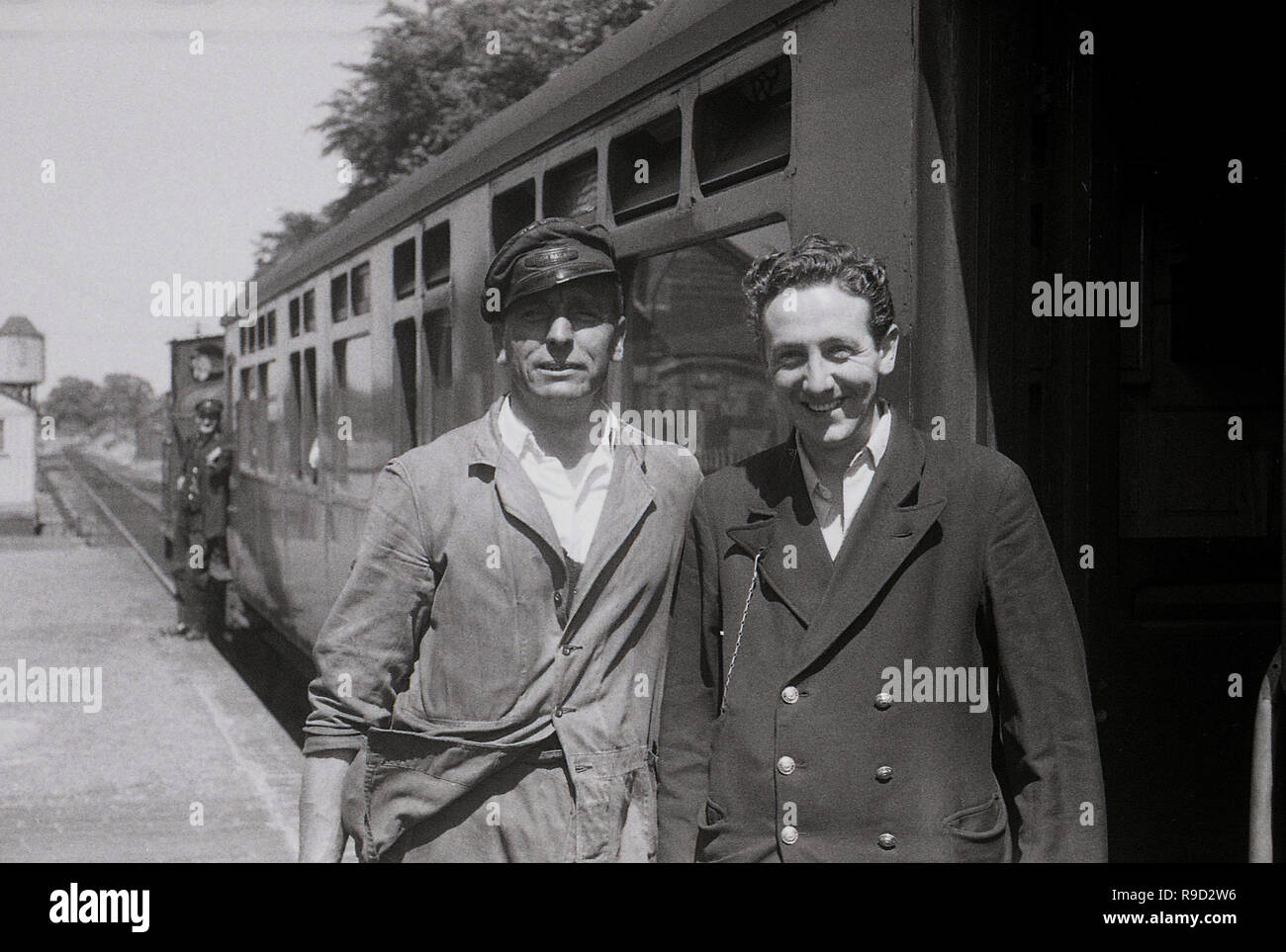 Années 1950, historiques, deux employés de chemins de fer britanniques, un conducteur de train d'une locomotive à vapeur dans son chapeau et garde un train, se tenir ensemble sur un quai de gare à l'extérieur d'un train, England, UK. British Railways a été la société d'État qui fonctionne hors-sol transport ferroviaire de 1948 jusqu'en 1997. En 1965, il est devenu connu sous le nom de British Rail. Banque D'Images