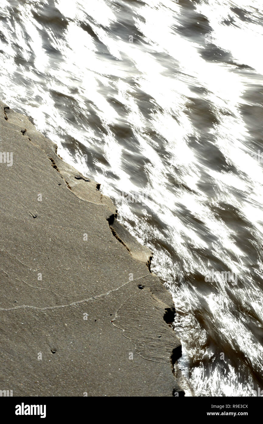 Le bord de la rivière de sable s'écroule comme la base est minée par l'eau qui coule Banque D'Images