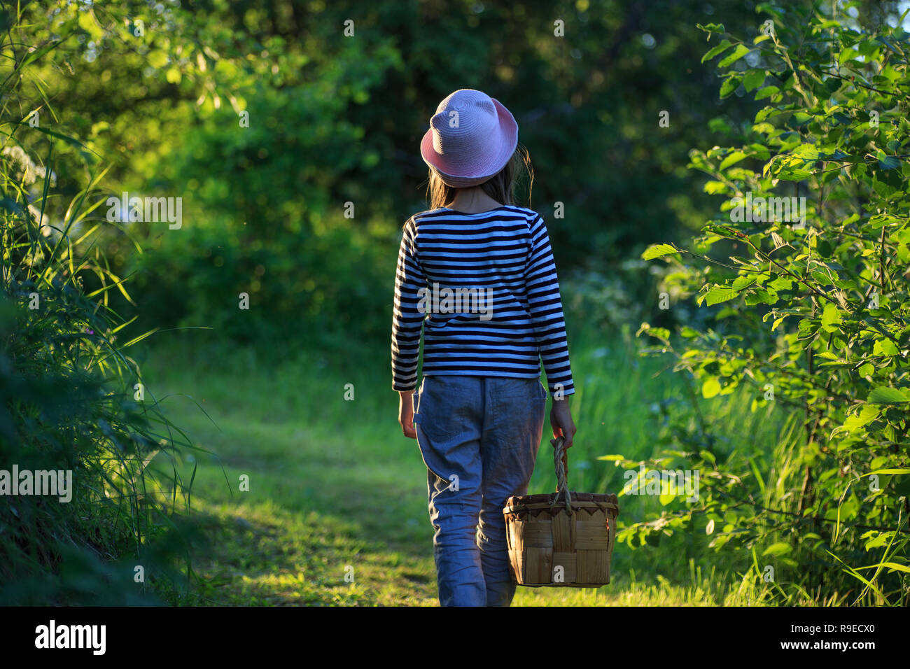 Jeune fille qui marche sur un chemin à travers bois verts portant un panier Banque D'Images