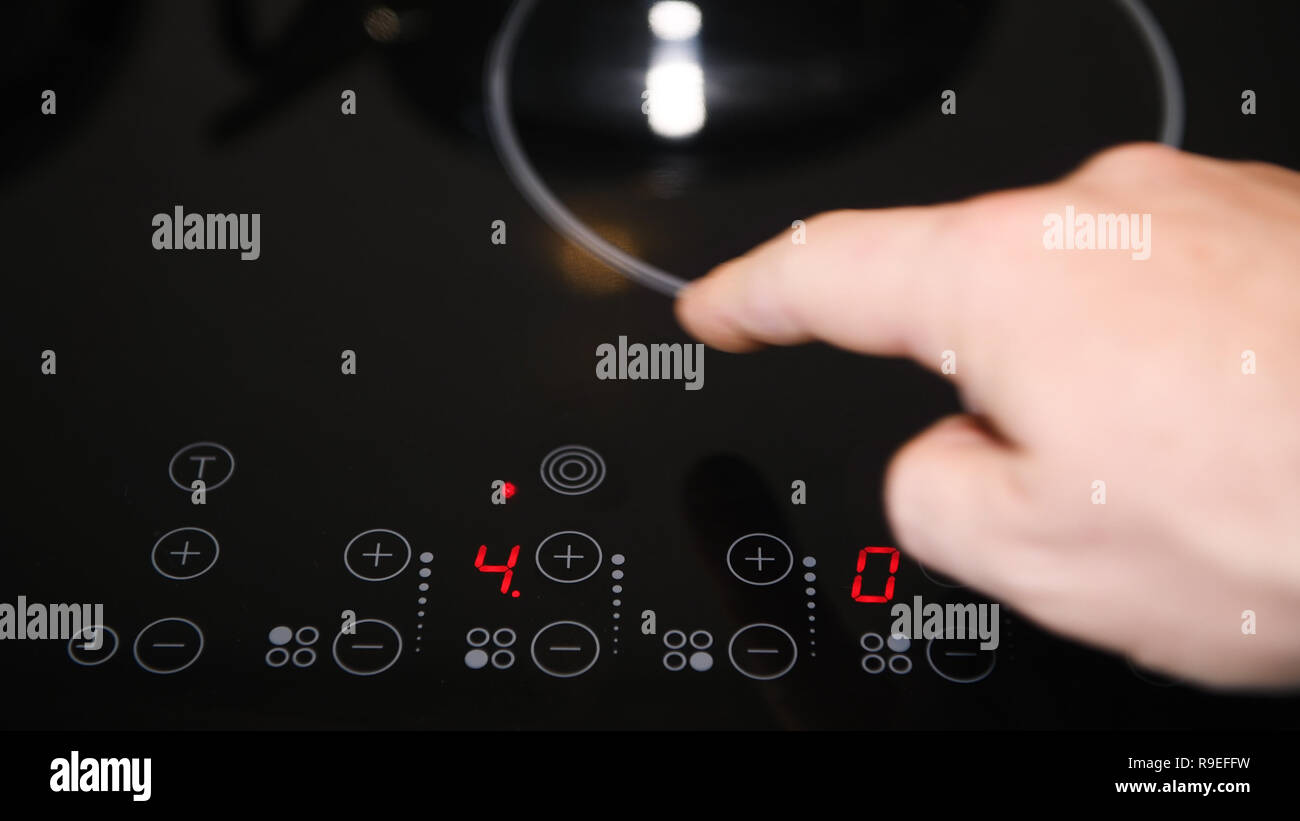 Close up de cuisinière électrique panneau de configuration, appuyer sur les boutons des doigts masculins, voyants rouges allumés Banque D'Images