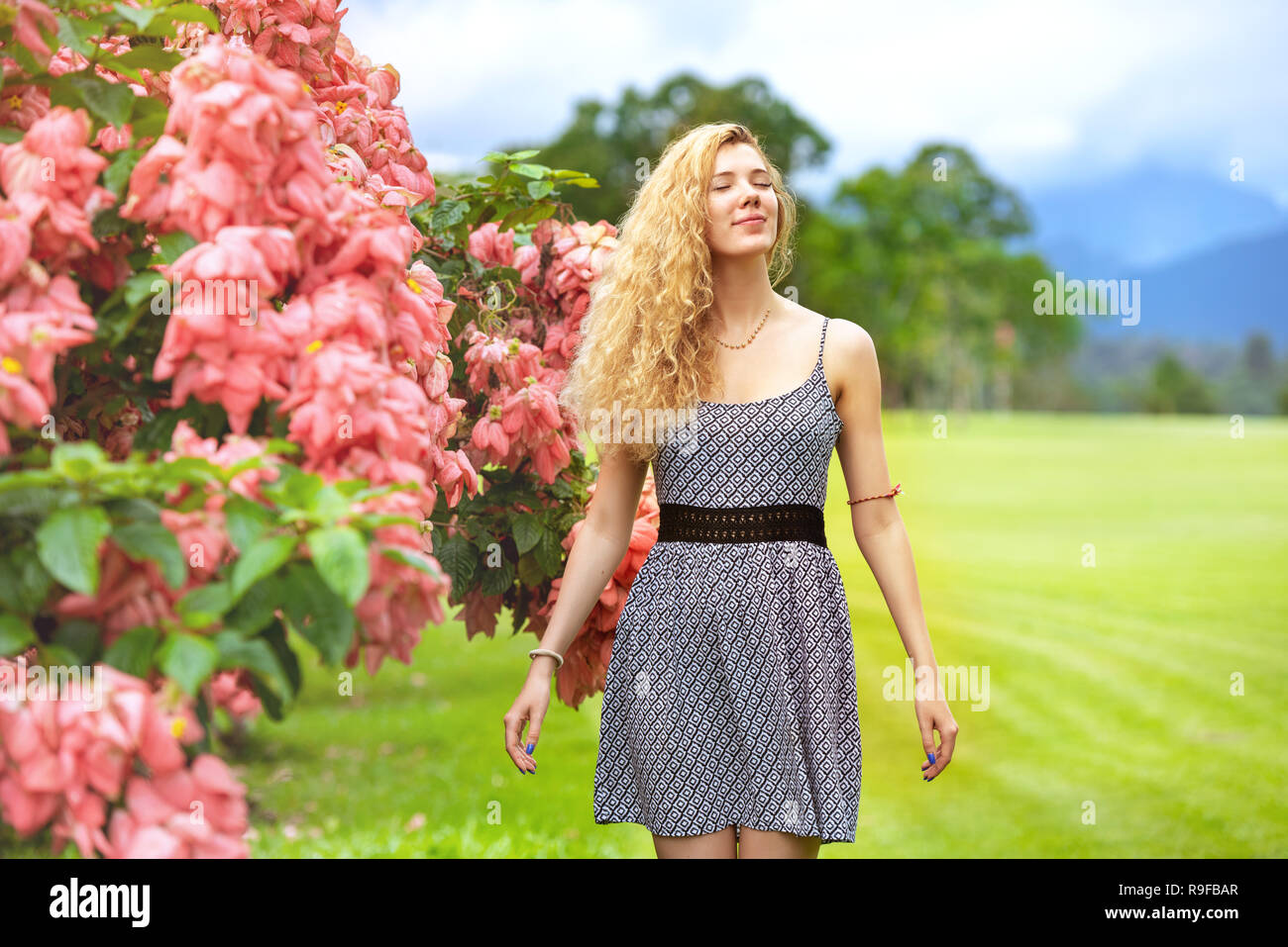 Heureux dame se tient près de bush avec des fleurs roses et bénéficie d Banque D'Images