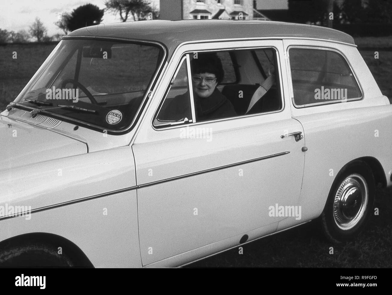 Années 1960, historiques, une femme assise dans le siège passager d'un 3-portes Austin A40 Farina voiture garée à l'extérieur de la fenêtre ouverte. Cette petite berline familiale voiture était badgée comme une Austin A40 Farina pour la distinguer des modèles précédents A40 et a été fabriqué entre 1958 -1967. Banque D'Images