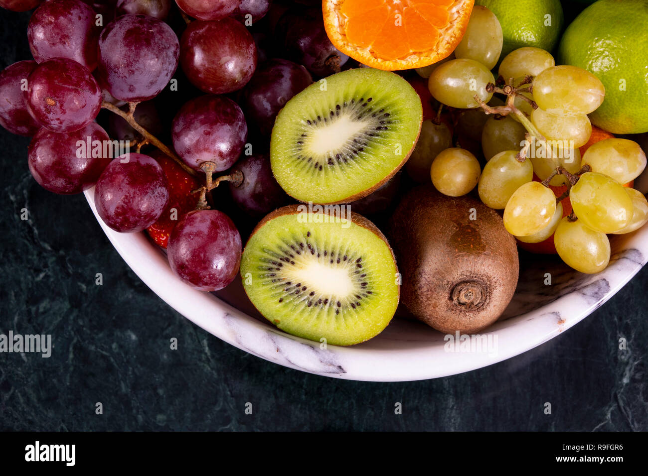 Fruitson tropicaux frais dans un bol sur le noir en arrière-plan. L'ananas, papaye, mangue, kiwi, raisin, grenat, mandarines, bananes, pommes, pastèque sli Banque D'Images