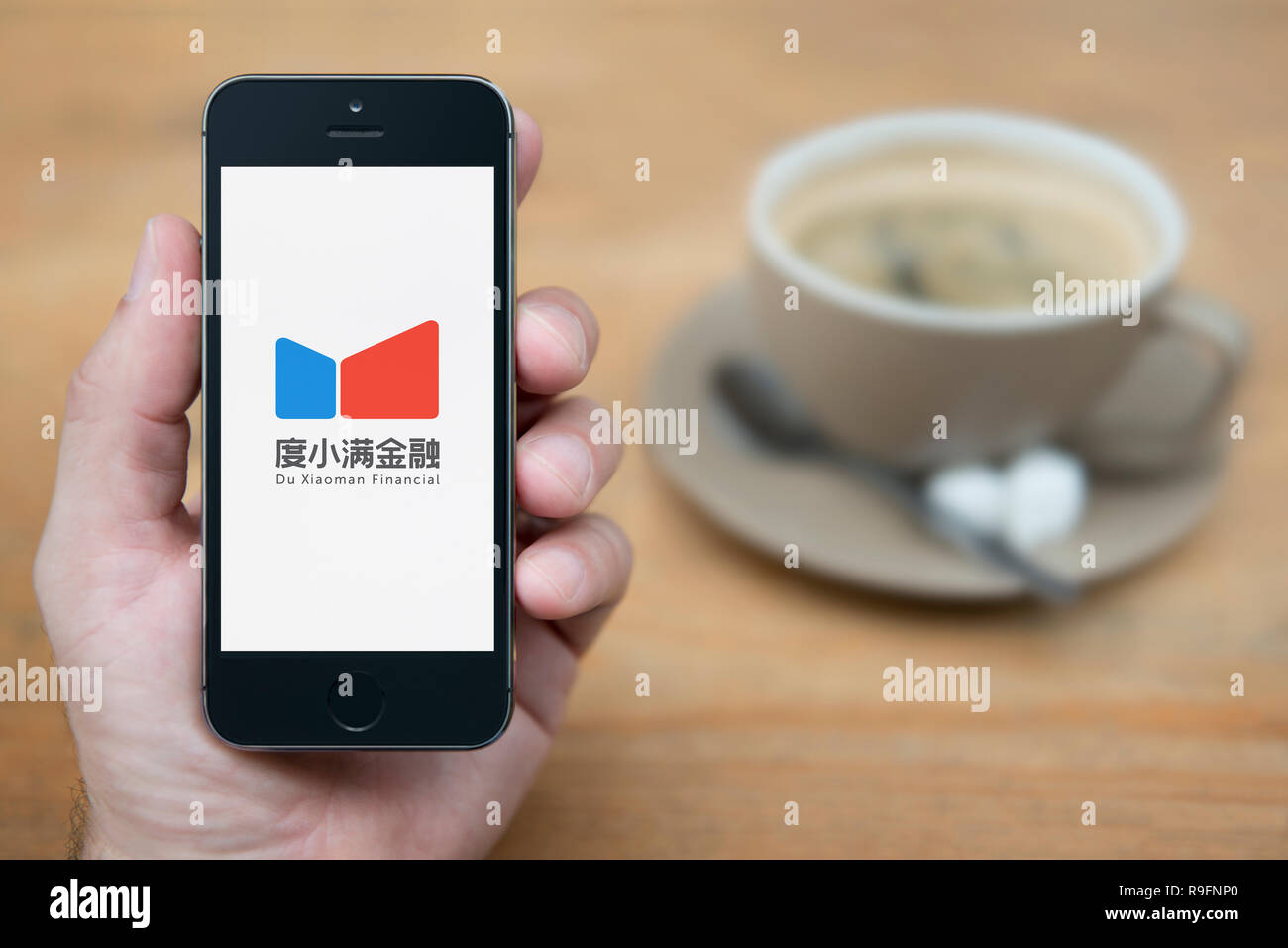 Un homme se penche sur son iPhone qui affiche le logo du financier Xiaoman (usage éditorial uniquement). Banque D'Images