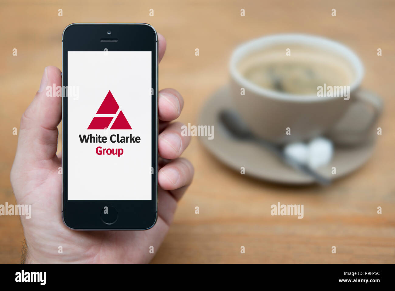 Un homme se penche sur son iPhone qui affiche le logo du groupe blanc Clarke (usage éditorial uniquement). Banque D'Images