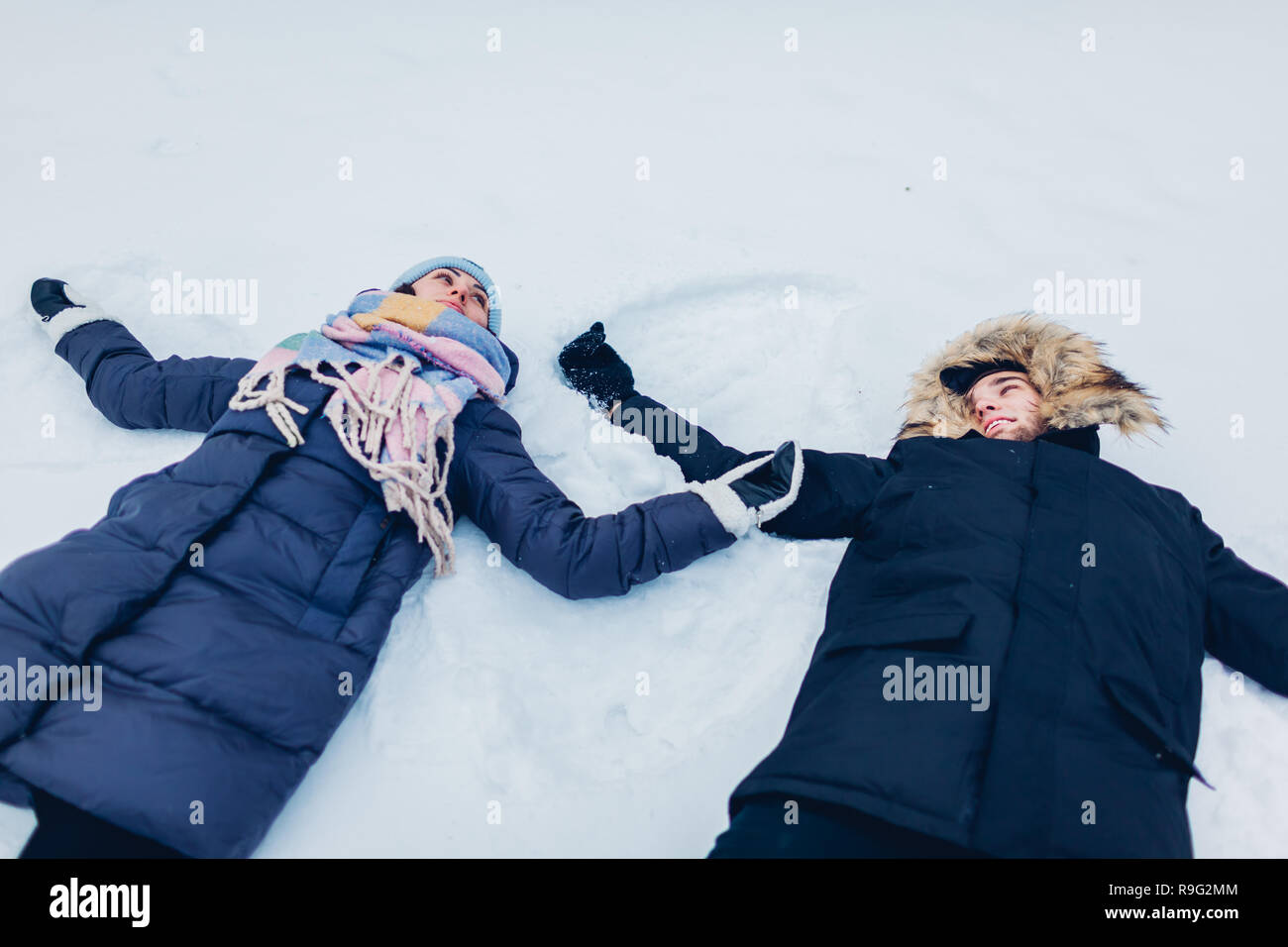 Beau couple aimant faire des anges dans la neige en hiver forêt couchée dans la neige. Les gens heureux s'amuser en plein air Banque D'Images
