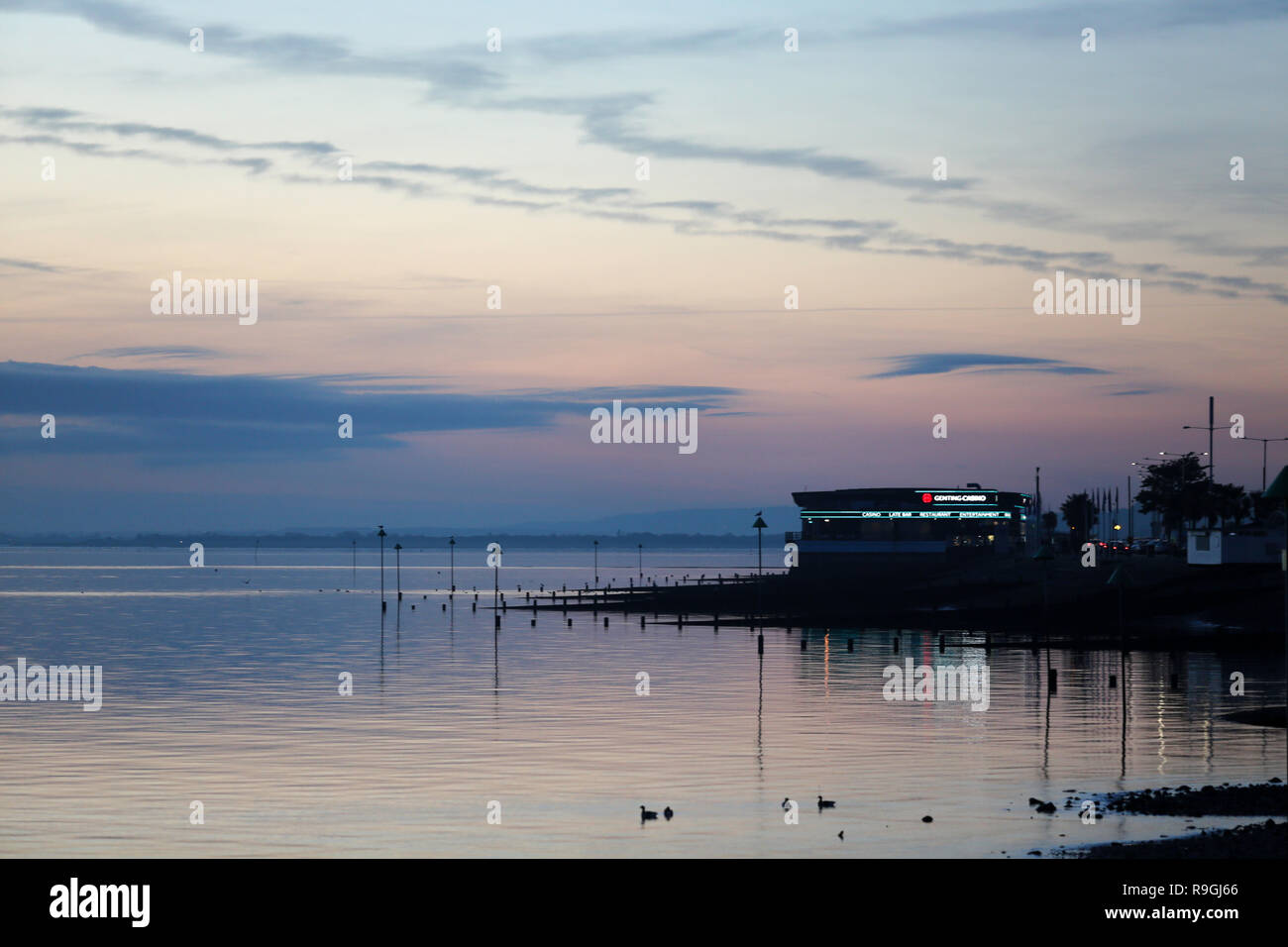 Southend, Southend on Sea, Royaume-Uni. 24 décembre 2018. Coucher de soleil sur la plage de Southend on Sea, sur l'estuaire de la Tamise. Une scène crépusculaire sereine le long de la côte britannique, avec des eaux calmes, des oiseaux silhouettes et un bâtiment côtier légèrement éclairé. Le ciel brille avec des teintes pastel de bleu, rose et violet, se reflétant sur la surface de l'eau. Les poteaux s'étendent dans la mer, ajoutant de la structure à la composition tranquille. Crédit : Penelope Barritt/Alamy Live News Banque D'Images