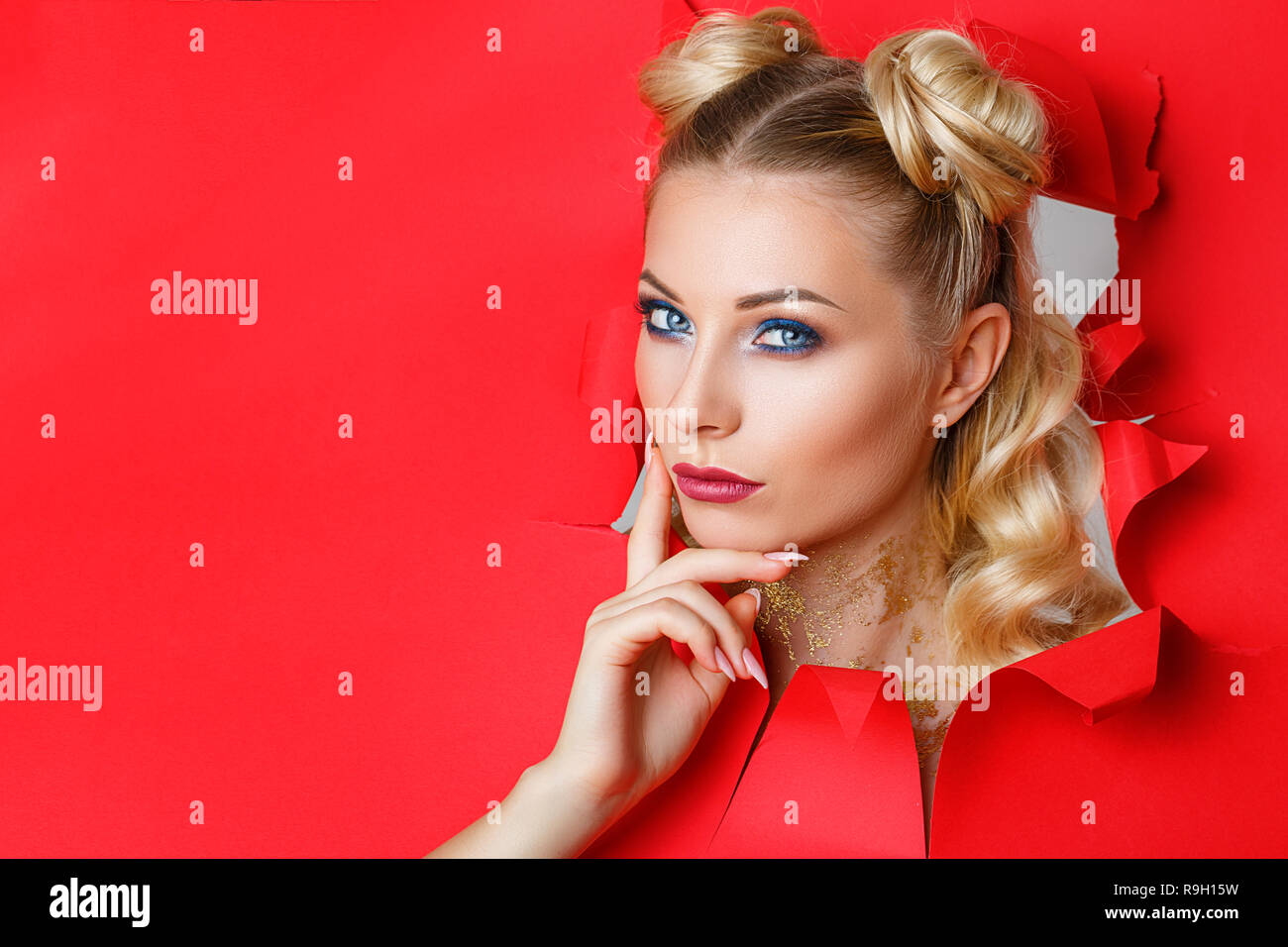 Une belle jeune fille en sort d'un trou dans du papier rouge, un beau  maquillage lumineux, les expressions du visage de surprise et d'intérêt  Photo Stock - Alamy