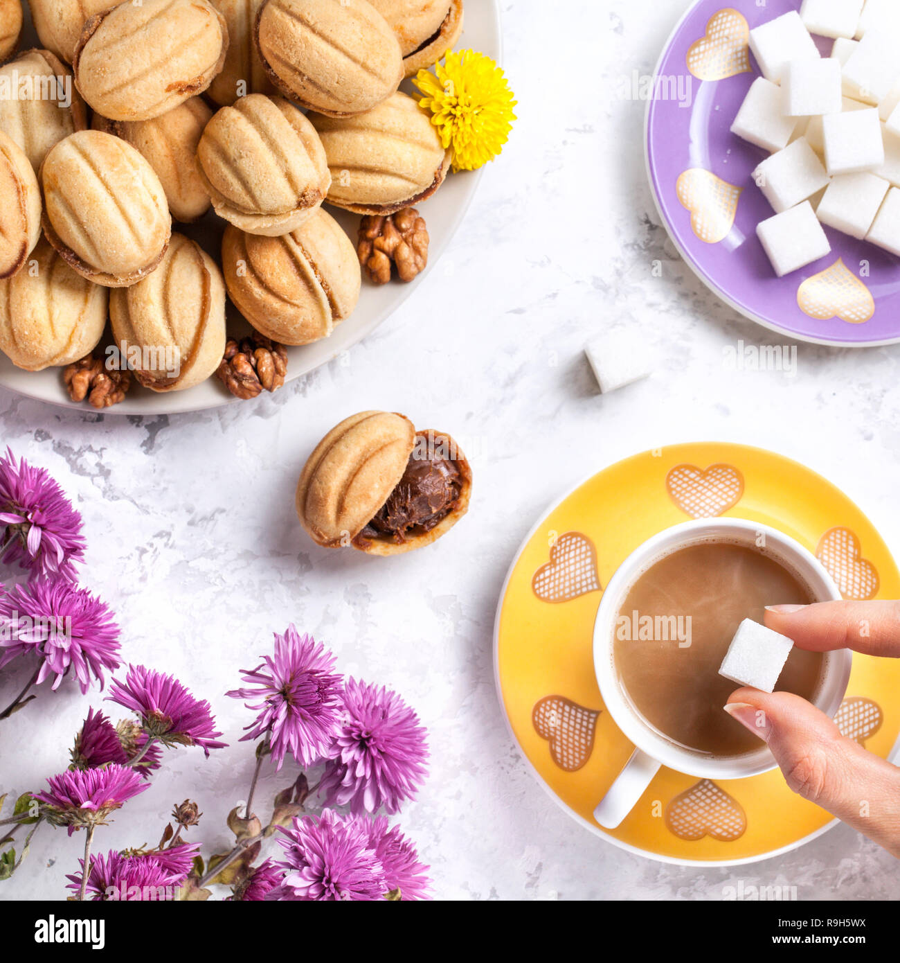 Mettre le sucre dans la main femme tasse de café près de sweet des écrous sur fond de marbre blanc Banque D'Images