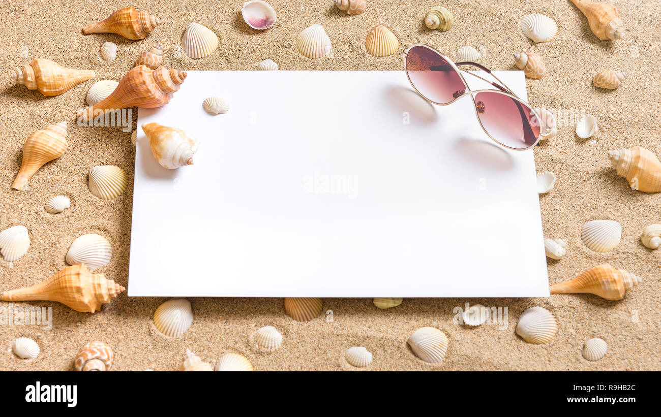 Carte blanche sur une plage de sable avec des coquillages et des lunettes de soleil, été plage locations theme Banque D'Images