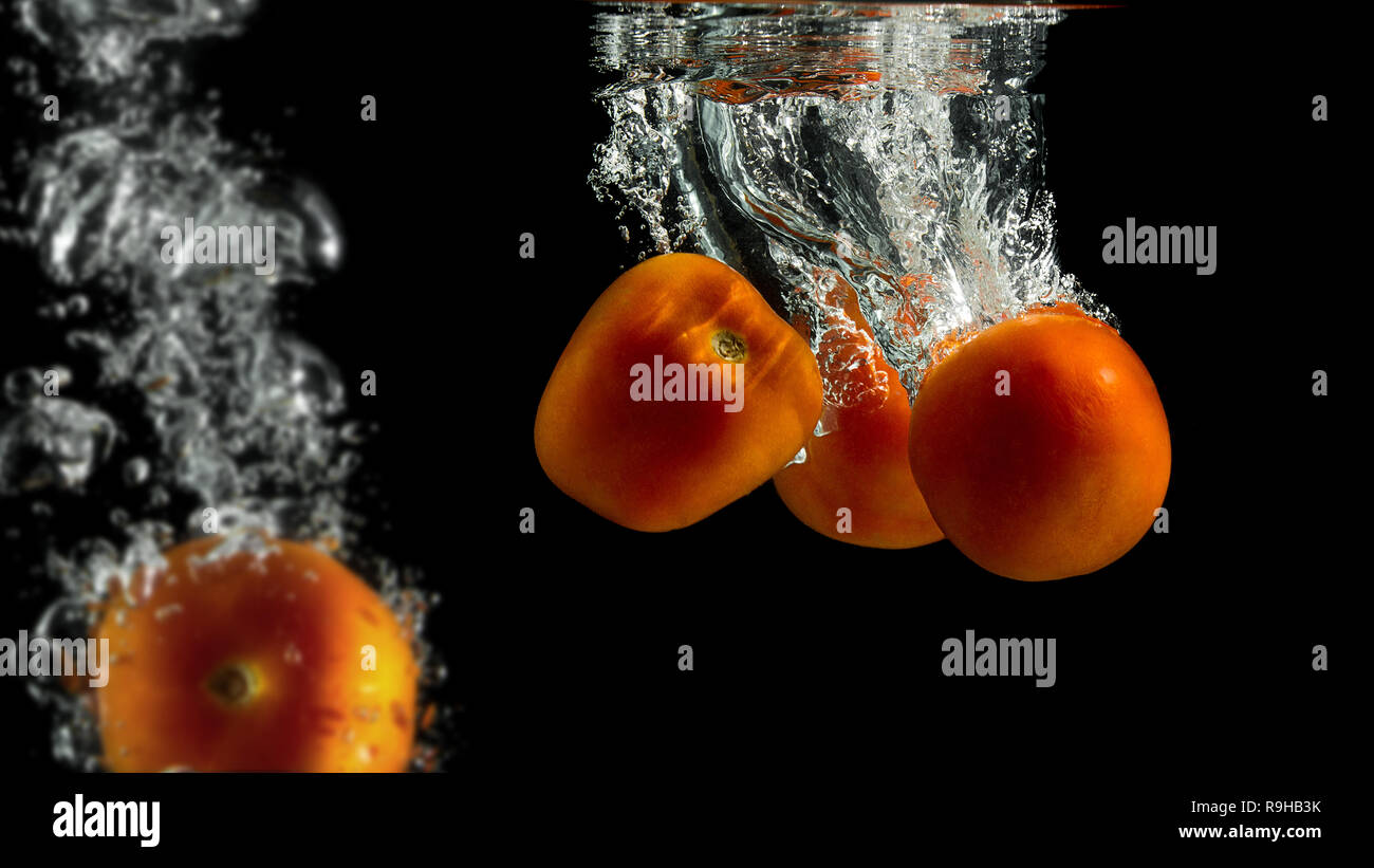 Les tomates biologiques les projections dans l'eau avec fond noir. Banque D'Images