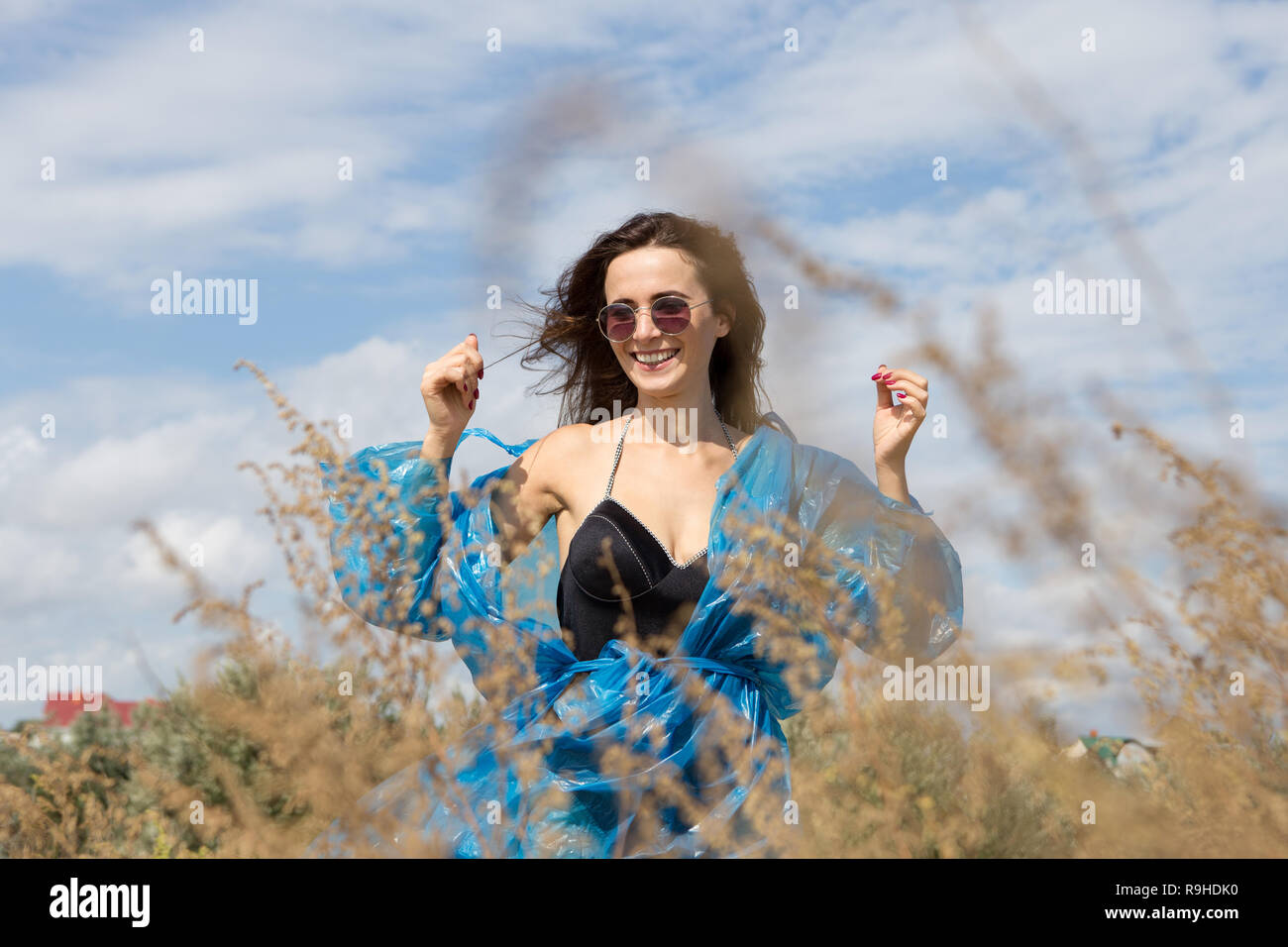 Portrait d'une jeune fille sexy debout sur un fond de ciel et d'herbes hautes. Elle porte un maillot noir, un manteau et des lunettes Banque D'Images