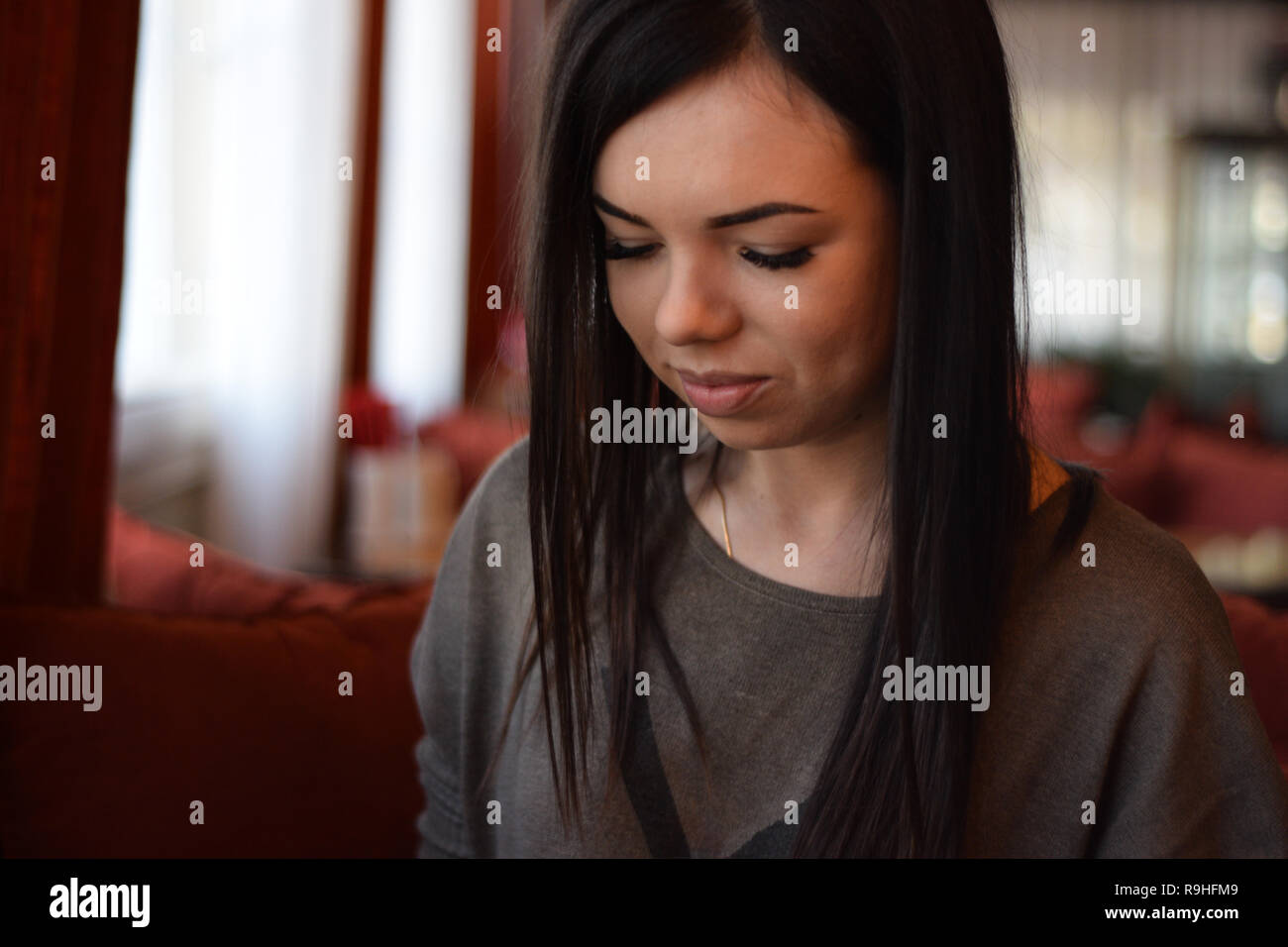 Portrait of a smiling belle fille avec des fossettes sur les joues dans un café confortable contre la fenêtre et bokeh. jeune femme est en train de lire un message dans la p Banque D'Images