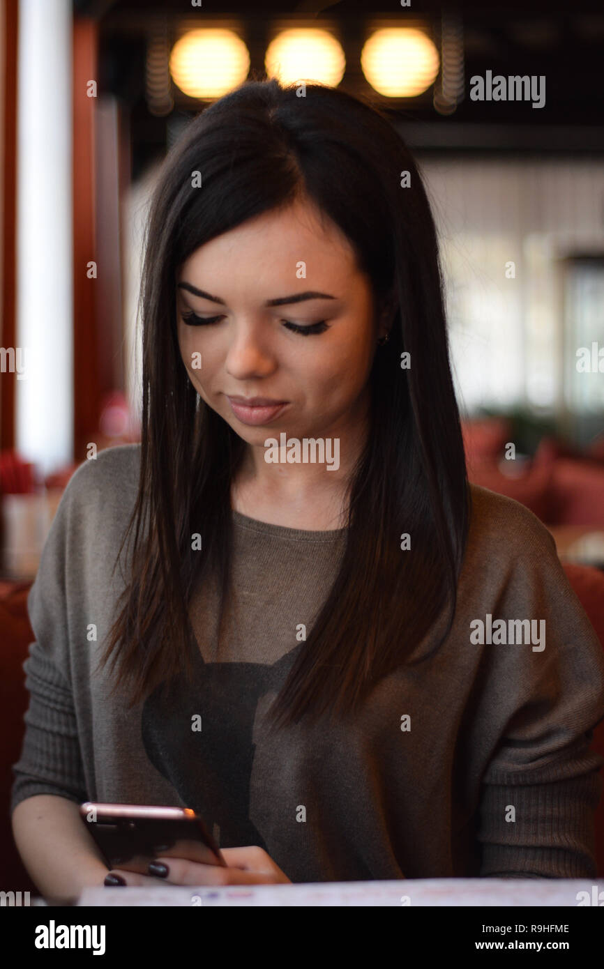 Portrait of a smiling belle fille avec des fossettes sur les joues dans un café confortable contre la fenêtre et bokeh. jeune femme est en train de lire un message dans la p Banque D'Images