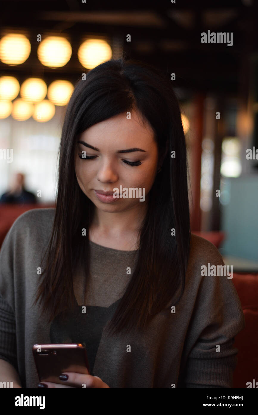 Portrait of a smiling belle fille avec des fossettes sur les joues dans un café confortable contre la fenêtre et bokeh. jeune femme est en train de lire un message dans la p Banque D'Images