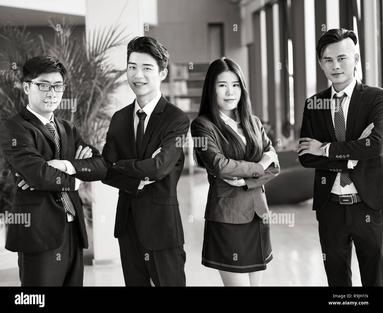 Portrait d'un groupe de jeunes gens d'affaires asiatiques standing in office les bras croisés, souriant, noir et blanc. Banque D'Images