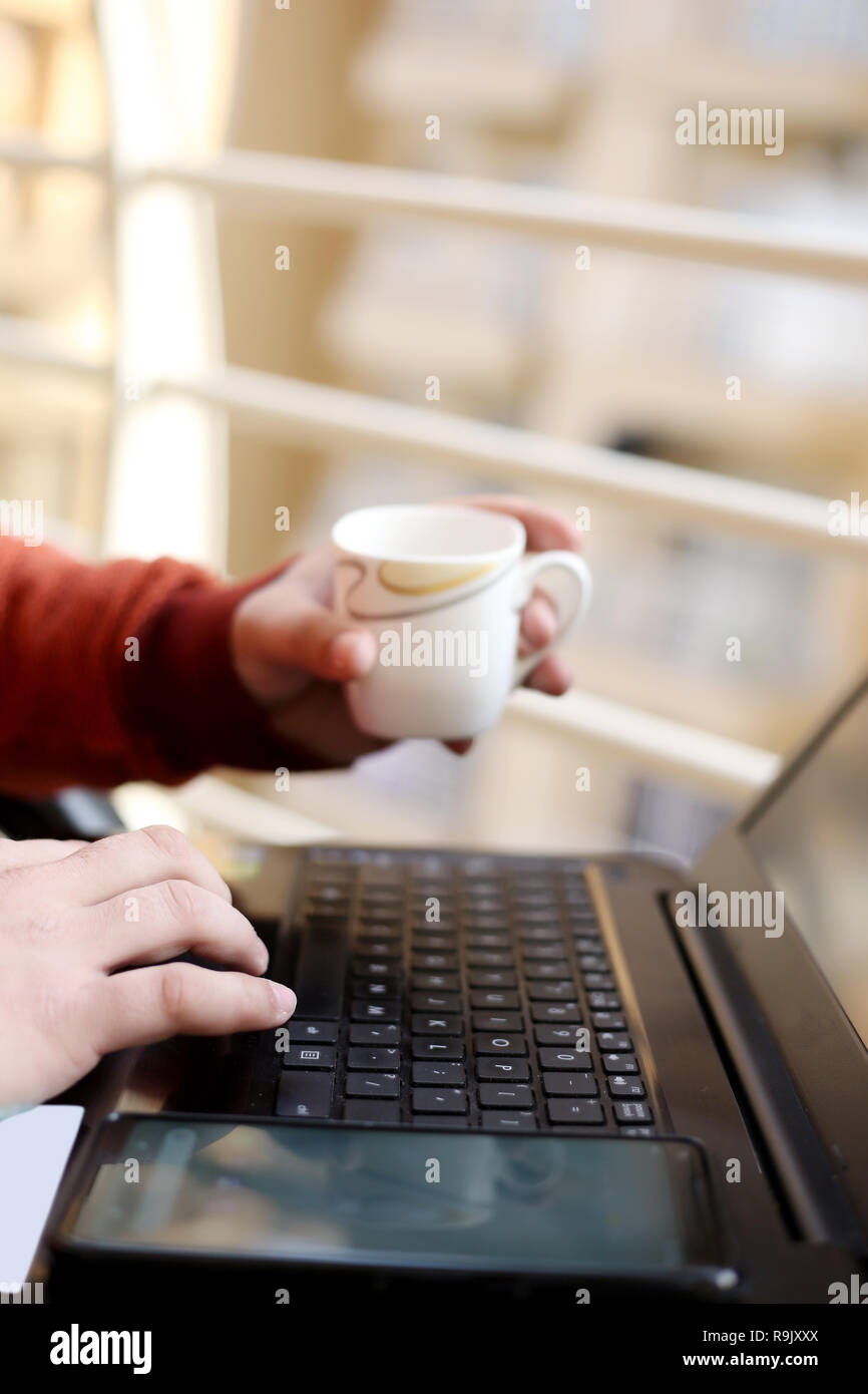 Jeune homme est à l'aide d'un ordinateur portable avec holding tasse de thé à la main. Banque D'Images