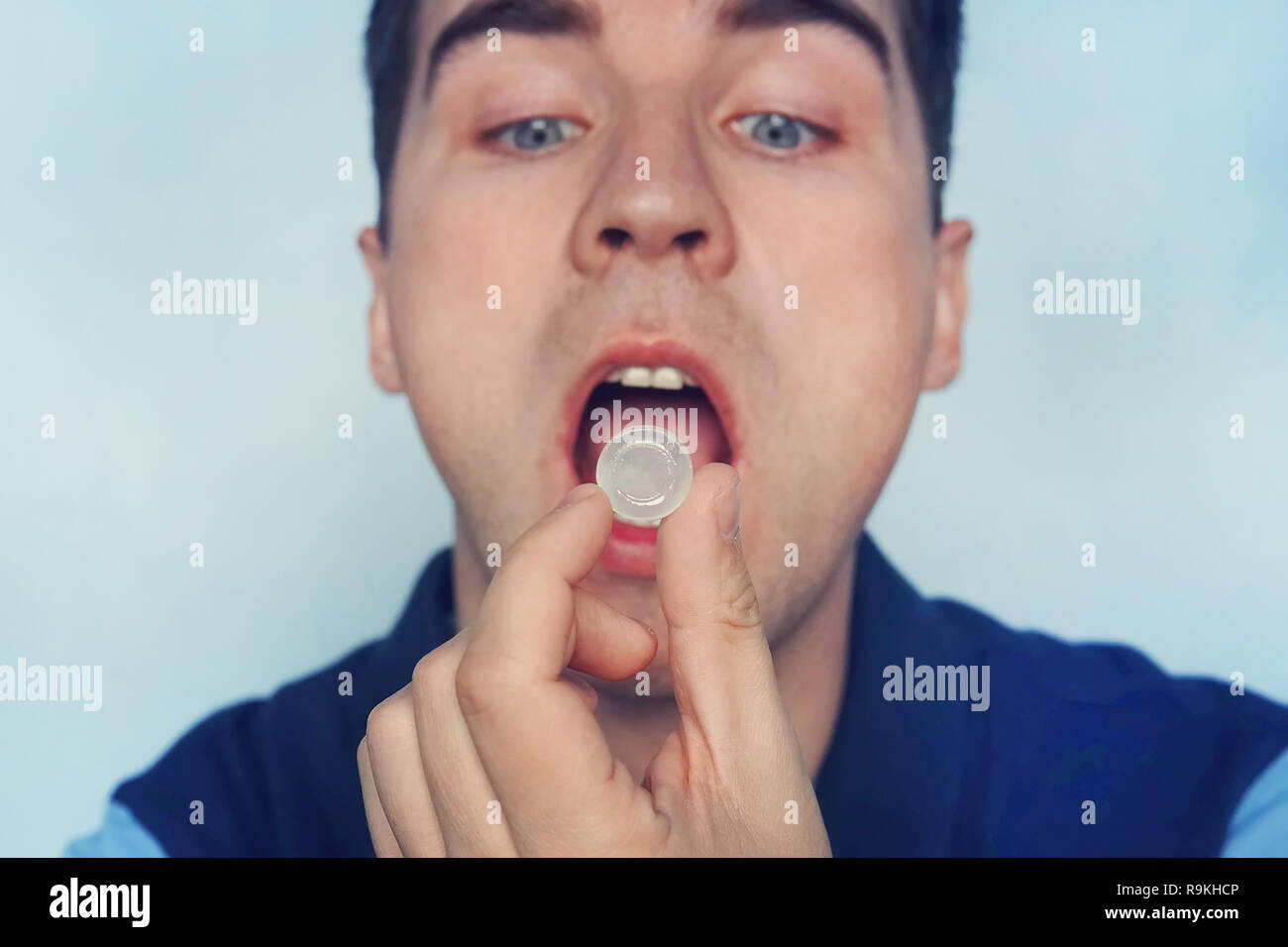 Jeune homme met dans sa bouche suçant un comprimé pour le mal de gorge. L'auto-médication pour la Grippe et rhume. Malade d'un mal de gorge, de menthe pour une haleine fraîche. Banque D'Images