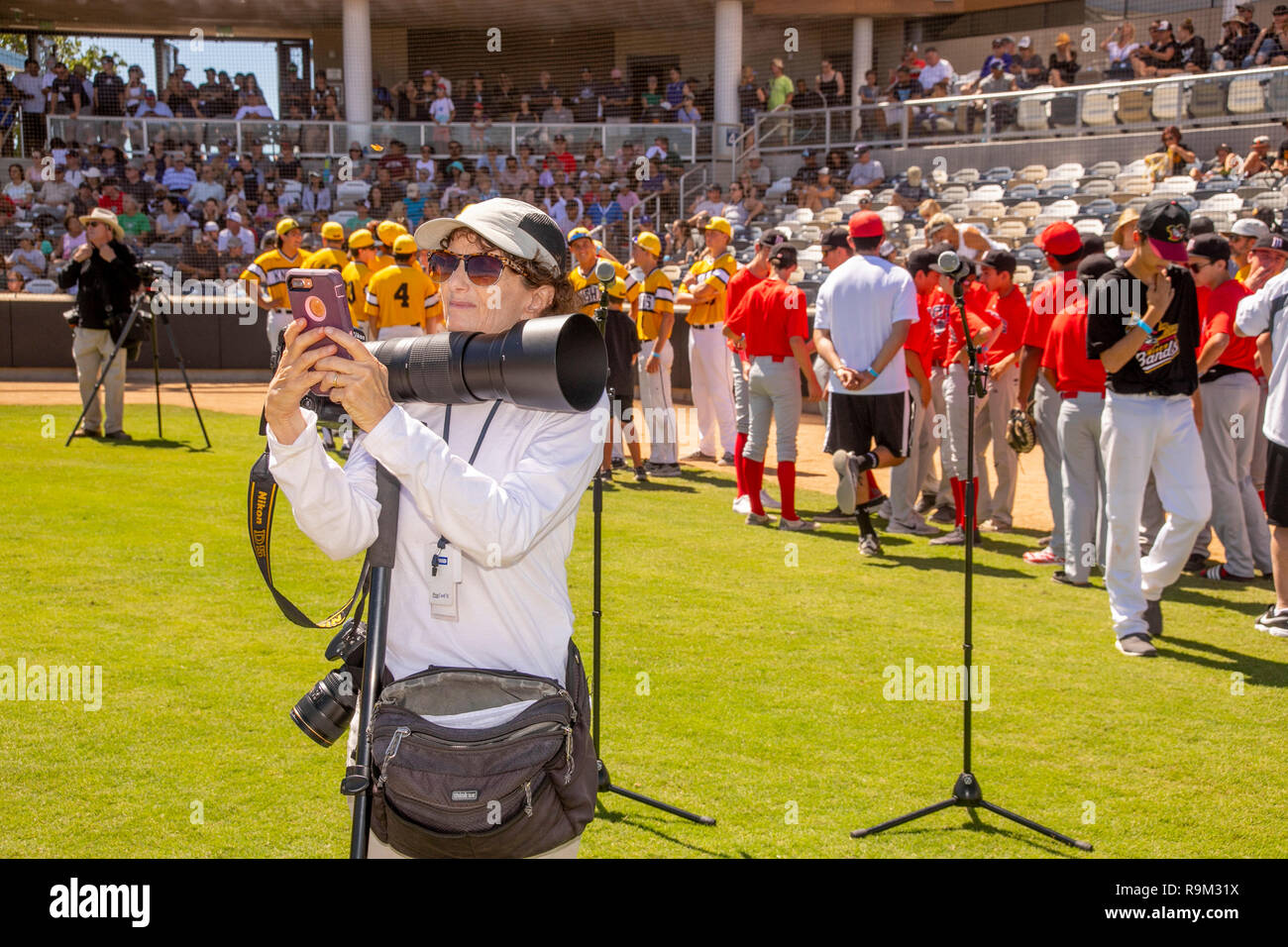 Avec une carte de presse autour de son cou, une femme photographe de presse vérifie son téléphone cellulaire alors qu'elle couvre un tournoi de softball à Irvine, CA. Banque D'Images