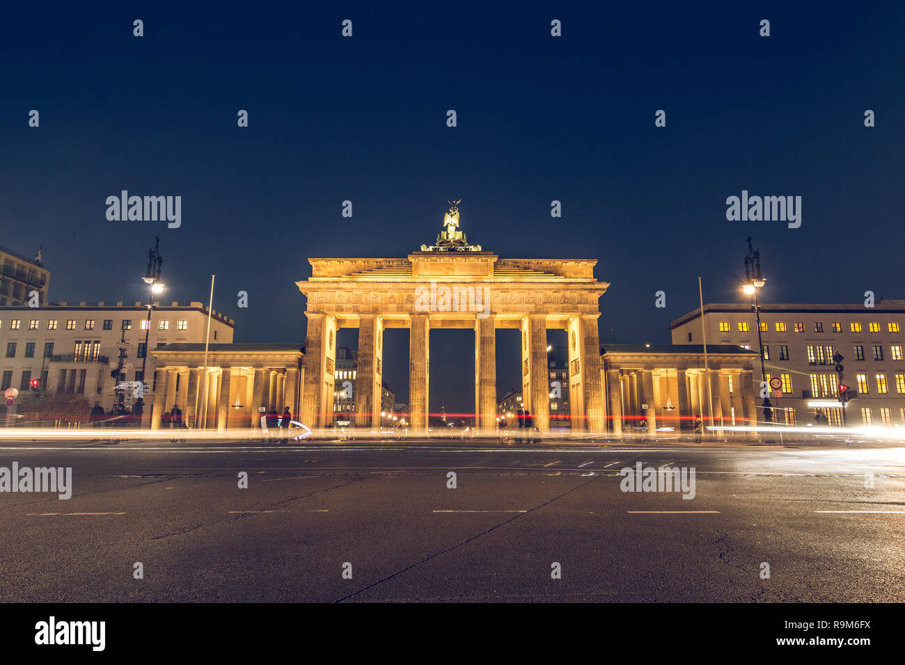 Porte de Brandebourg de Berlin de nuit avec vue arrière. Lanternes illuminent la rue. Lumière de voitures passant est visible. Le monument est allumé Banque D'Images