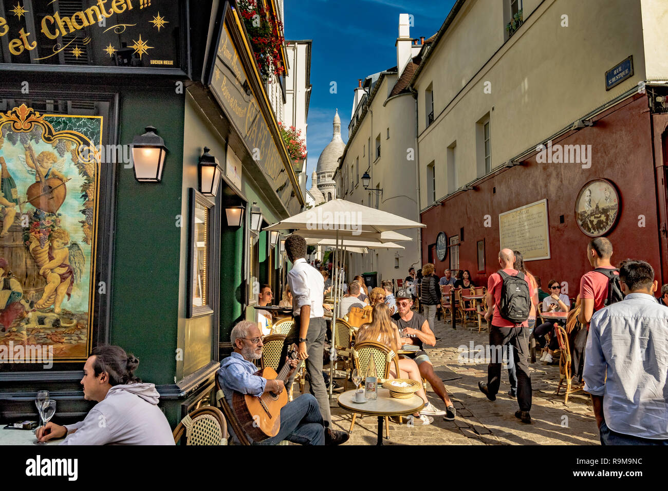 Un homme assis jouant de la guitare à l'extérieur de La Bonne Franquette, un café, restaurant, tandis que les gens profiter d'un déjeuner au soleil, Montmartre, Paris Banque D'Images