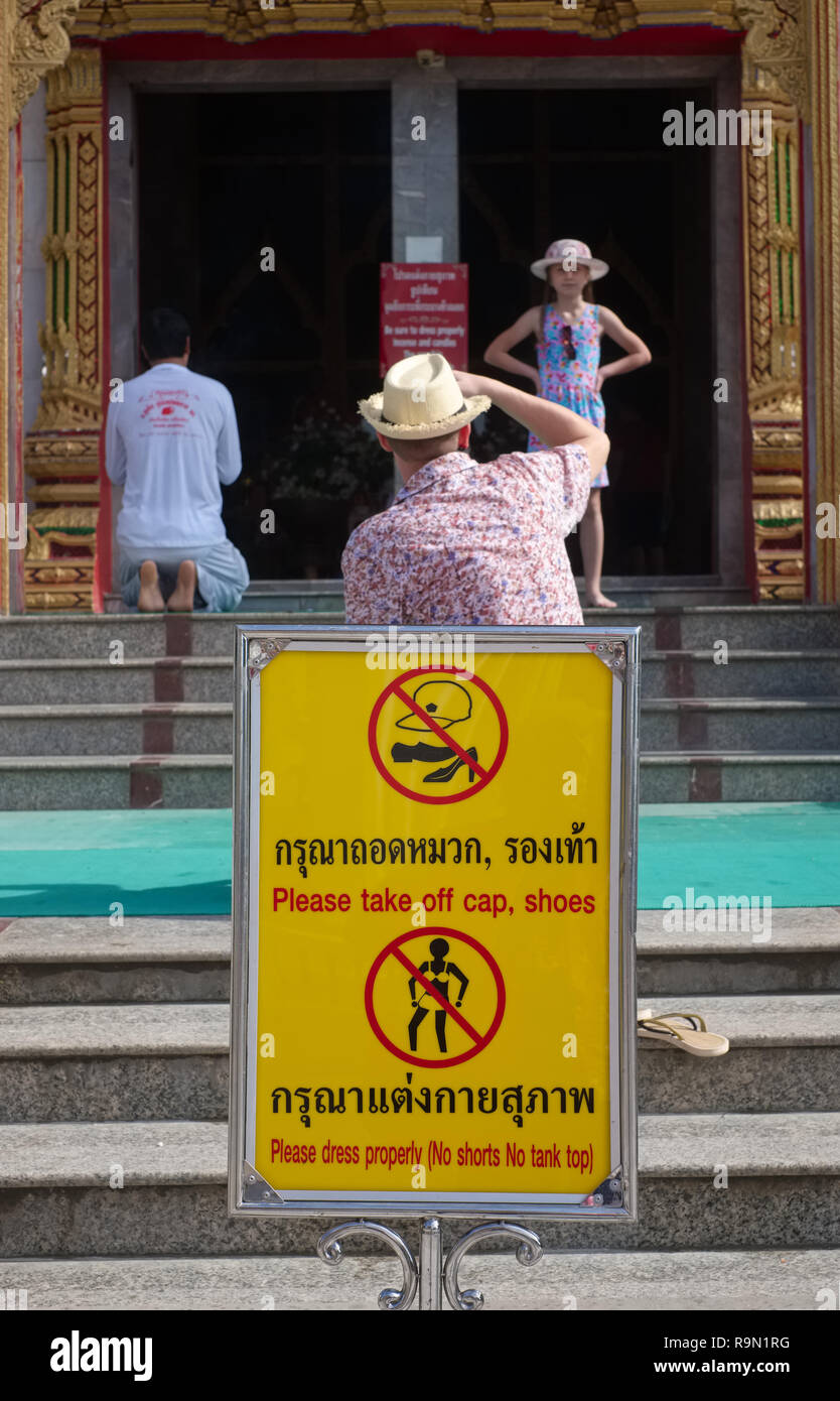 Un avis au Wat Chalong, Phuket, Thailande annonçant la tenue de rigueur pour entrer dans le temple, qu'à être ignorés par les touristes photographiant derrière Banque D'Images