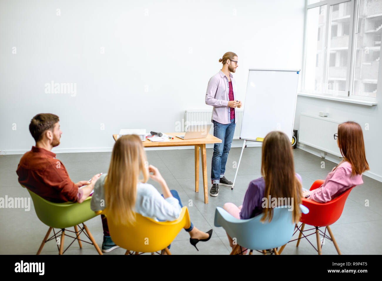 Jeune homme en tant qu'un orateur déclaration à l'audience au cours de la réunion dans la salle de conférence avec des chaises colorées Banque D'Images