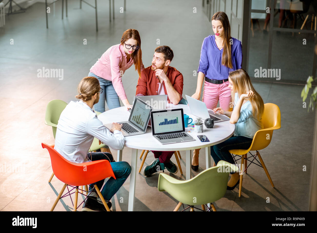 Une équipe de jeunes collègues habillés de désinvolture qui travaillent ensemble avec des ordinateurs portables assis à la table ronde de l'office Banque D'Images