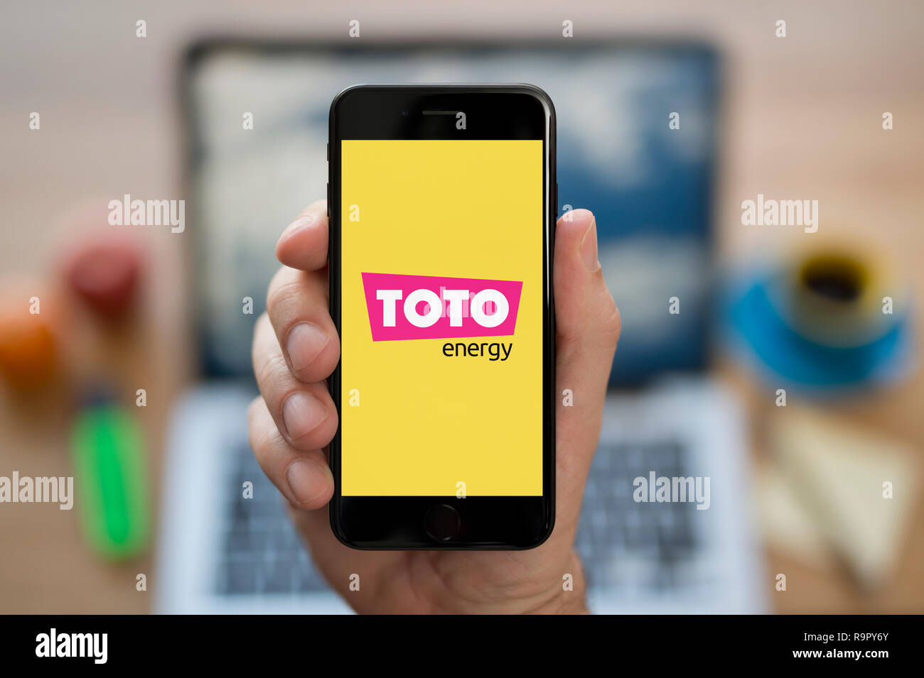 Un homme se penche sur son iPhone qui affiche le logo de l'énergie Toto  (usage éditorial uniquement Photo Stock - Alamy
