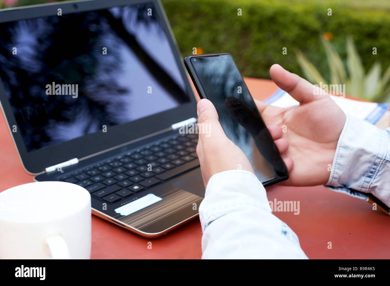 Photo de l'homme main est l'utilisation de smartphone avec ordinateur portable et tasse sur la table. Banque D'Images