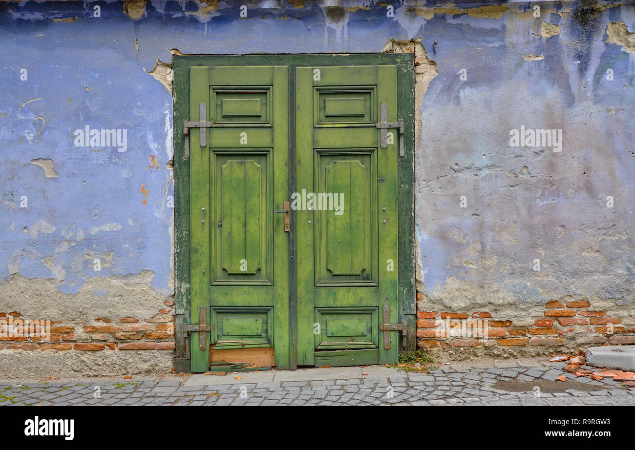 Siècle bleu en ruine ancienne paroi plus de brique, avec un panneau de porte de remorquage en bois vert Banque D'Images