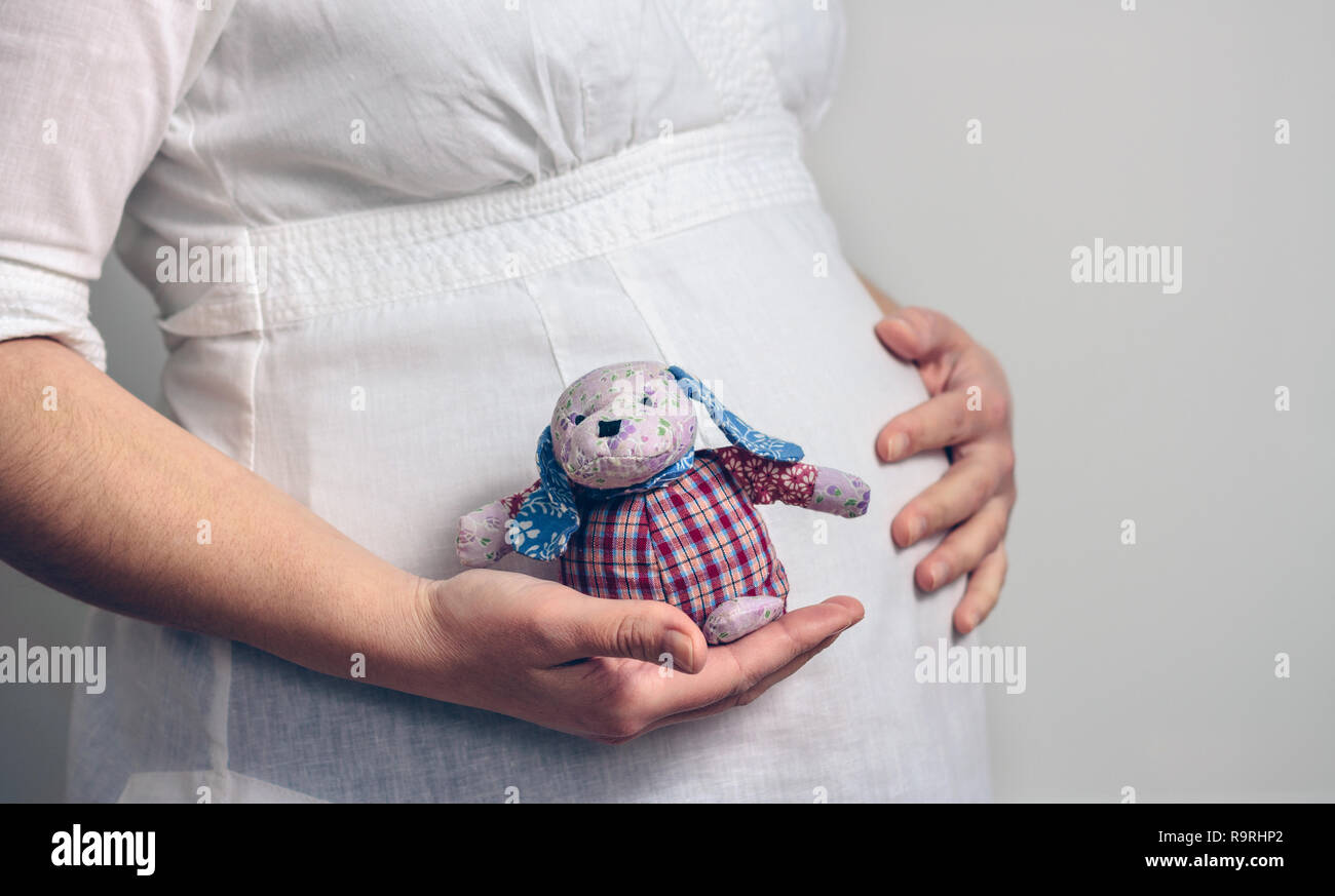Ventre de femme enceinte tenant un bébé poupée de chiffon Banque D'Images