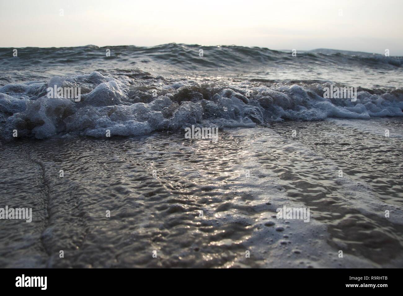 Une ligne de petites vagues genoux une plage que la marée se retire, le curling le sable et faire des bulles sale mélangée à de la mousse blanche et propre, comme grosses vagues buil Banque D'Images