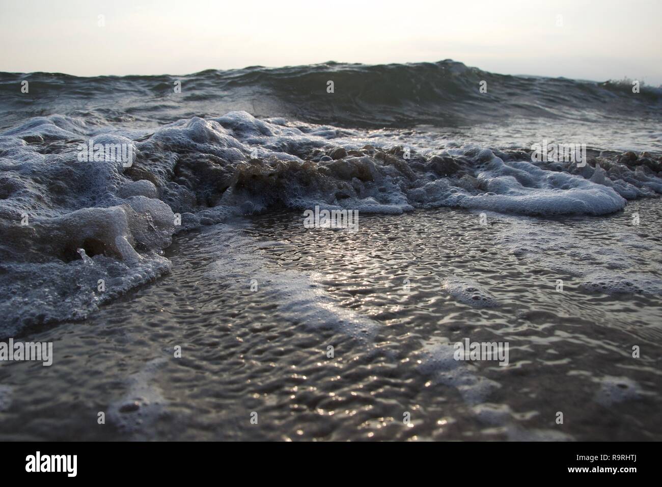 Petites vagues genoux une plage que la marée se retire, le curling le sable et faire des bulles sale mélangée à de la mousse blanche et propre, comme grosses vagues construire dans la b Banque D'Images
