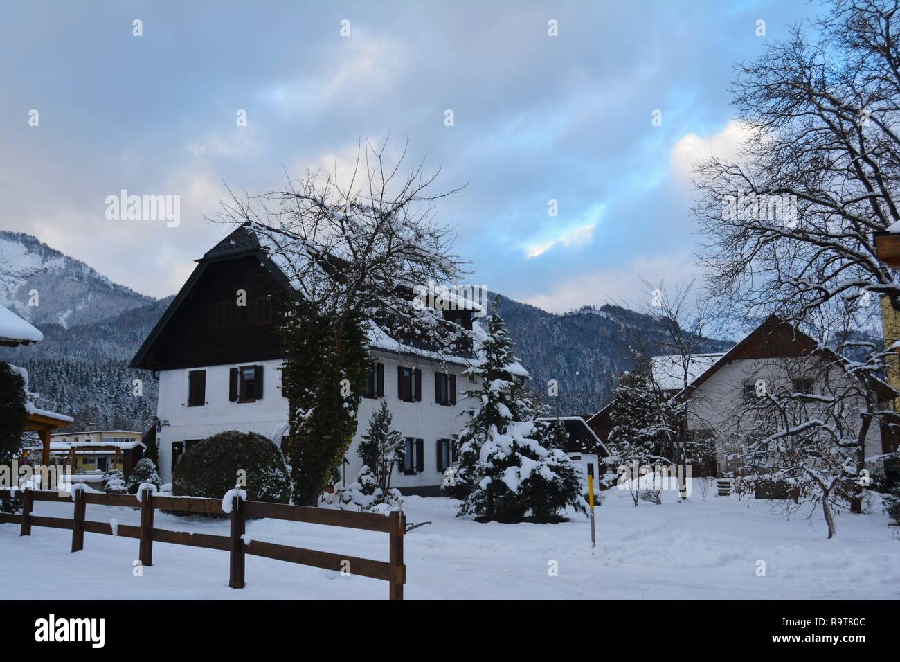 Un pittoresque maison en bois couverte de neige à Bad Goisern, Hallstatt, Autriche. Ciel nuageux Ciel bleu et les montagnes enneigées en arrière-plan. Banque D'Images