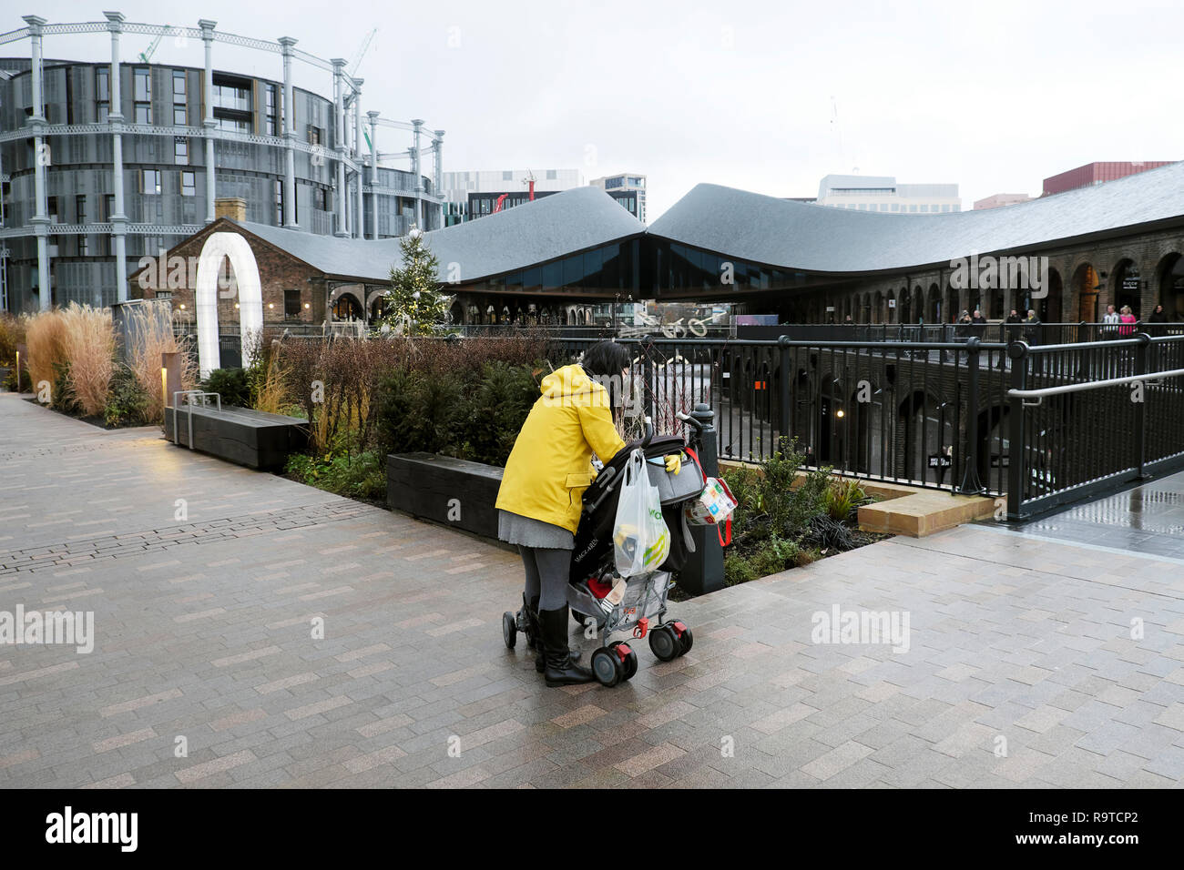 Vue arrière d'une femme et d'une poussette avec les sacs et une vue gazomètres immeuble et le charbon tombe Yard Kings Cross Londres UK KATHY DEWITT Banque D'Images