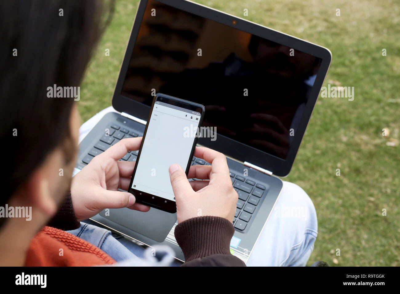 Garçon travaille sur le smartphone avec un ordinateur portable. Banque D'Images
