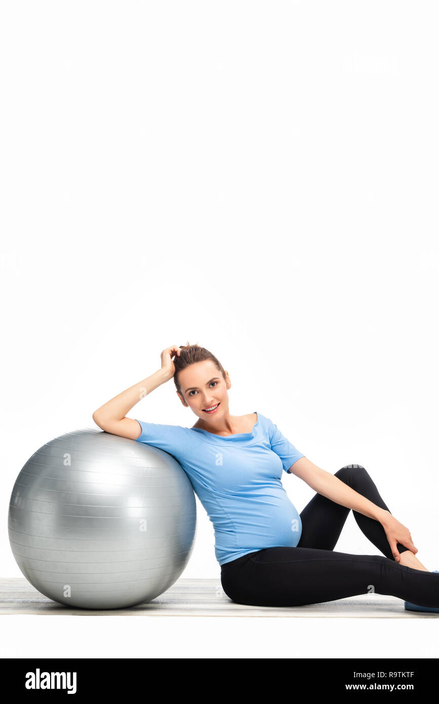 Brown haired pregnant woman sitting on floor with fitness ball et à la caméra de isolated on white Banque D'Images