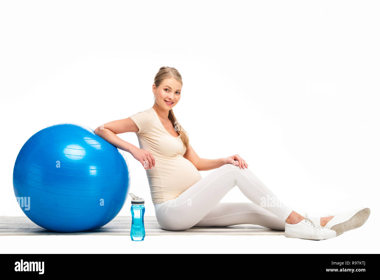 Enceinte blonde woman sitting on floor with blue fitness ball isolated on white Banque D'Images