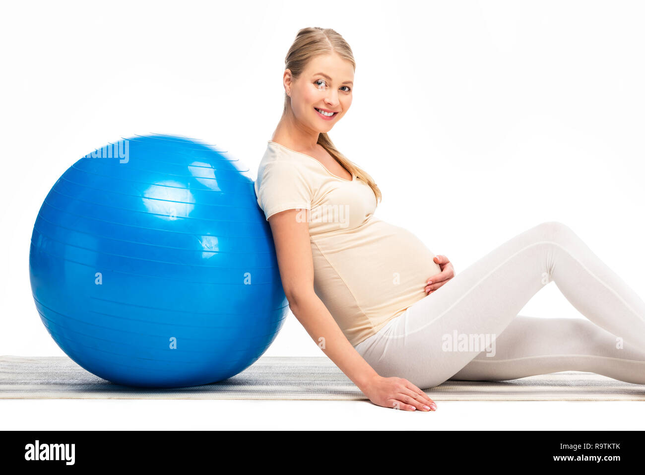 Smiling pregnant woman leaning on blue fitness ball isolated on white Banque D'Images