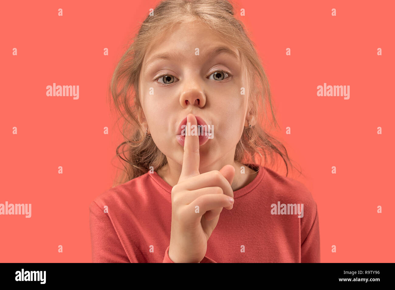 Jeune fille avec son doigt sur sa bouche sur fond de corail. Les émotions humaines et l'expression faciale plus de couleur à la mode Banque D'Images